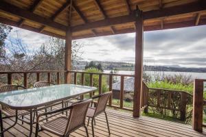 um alpendre com uma mesa de vidro e cadeiras num deque em Apart hotel Puchaley Lafquen em Panguipulli