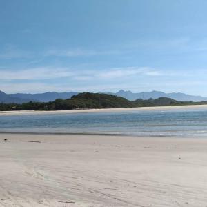 a beach with the ocean and mountains in the background at BertAkua in Bertioga