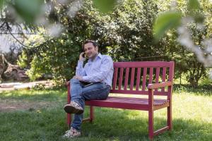 Un uomo seduto su una panchina che parla al cellulare di Apartments Villa Anita a Bolzano