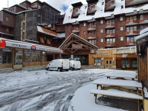 een met sneeuw bedekte straat met auto's geparkeerd voor een gebouw bij L'Ours Blanc in Huez