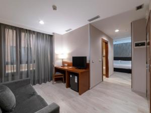 ein Wohnzimmer mit einem Sofa und einem Schreibtisch mit einem TV in der Unterkunft Hotel Plaza Las Matas in Las Rozas de Madrid