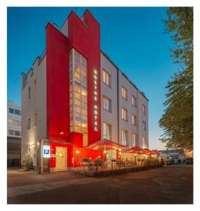 un bâtiment rouge avec des tables et des parasols devant lui dans l'établissement Goethe Hotel Messe by Trip Inn, à Francfort-sur-le-Main