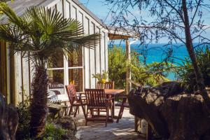 eine Terrasse mit einem Tisch, Stühlen und Meerblick in der Unterkunft Te Hapu Coastal Cottages in Collingwood