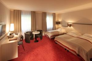 a hotel room with two beds and a desk at Bergers Airporthotel Memmingen in Memmingerberg