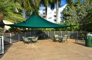 un patio con mesa, sillas y una sombrilla verde en Sunrise Suites Dominican Suite #110, en Key West