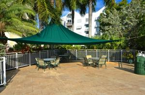 eine Terrasse mit einem Tisch, Stühlen und einem grünen Sonnenschirm in der Unterkunft Sunrise Suites Dominican Suite #110 in Key West