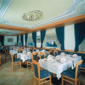 een restaurant met witte tafels en stoelen en een kroonluchter bij Piccolo Hotel in Canazei