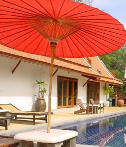 een rode paraplu op een tafel naast een zwembad bij Sea Pines & Liberg in Nai Yang Beach