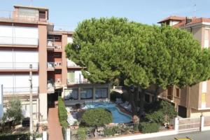 a large tree in front of a building with a swimming pool at Hotel Kristall in Diano Marina