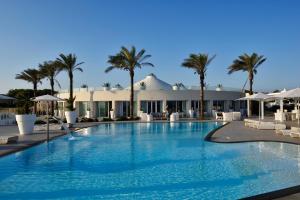 a large swimming pool with palm trees and a building at Sole in me Resort by Altoborgo in Ostuni