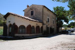 um antigo edifício de pedra com portas e janelas numa estrada de terra em La Locanda sul Lago em Santo Stefano di Sessanio