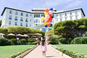 a little girl holding balloons in front of a building at Grand-Hôtel du Cap-Ferrat, A Four Seasons Hotel in Saint-Jean-Cap-Ferrat