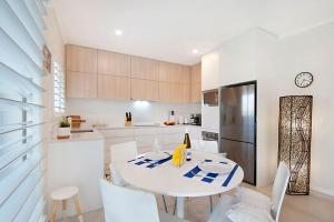 a white kitchen with a table and chairs and a refrigerator at Durramboi Luxury Apartment in Noosaville