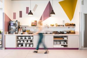 a woman walking past a counter in a coffee shop at Aparthotel Adagio access München City Olympiapark in Munich
