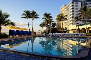 a swimming pool with chairs and palm trees and a building at Ocean Sky Hotel & Resort in Fort Lauderdale