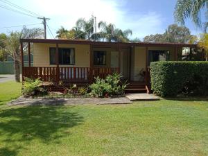 una pequeña casa amarilla con porche y patio en Leisure Tourist Park, en Port Macquarie