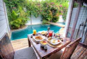 a table with breakfast food on it next to a swimming pool at Atoll Haven Villas in Gili Islands