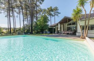 una piscina di fronte a una casa con palme di Madame Vacances Les Dunes de la Prade a Moliets-et-Maa