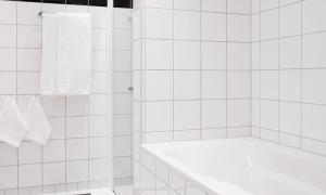 a white tiled bathroom with a tub and a towel at Thon Hotel Opera in Oslo