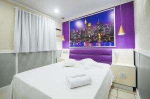a room with a white bed with a purple wall at Calamares Hotel São Caetano in São Caetano do Sul
