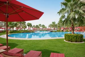 
a patio area with a pool, lawn chairs, and a red umbrella at Khalidiya Palace Rayhaan by Rotana, Abu Dhabi in Abu Dhabi
