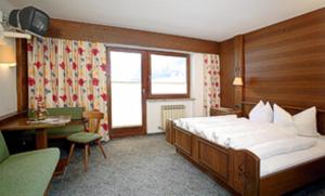 ゼルデンにあるAlpenheim Mathiasのベッド、デスク、ベッドサイドシックスが備わるホテルルームです。