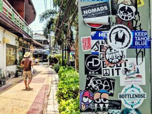 Un uomo che cammina per strada con degli adesivi su un muro di Lucky Dorm a Phi Phi Don