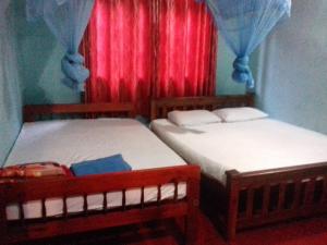 two beds in a room with a window with red curtains at Thisal Guest House in Polonnaruwa