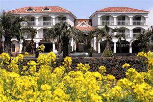 a large white house with palm trees and yellow flowers at MJ Pension & Resort in Seogwipo