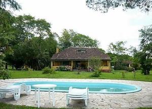 a pool with chairs and a table and a house at Pousada Chácara das Roseiras in Bagé