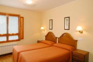 1 dormitorio con 2 camas con sábanas de color naranja y ventana en Hotel Restaurante El Manquin, en Villaviciosa