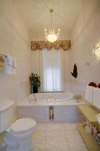 baño con bañera, aseo y lámpara de araña. en Amethyst Inn, en Victoria