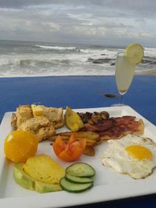 a plate of breakfast food with a drink and the ocean at Milkwood Beach Cottages in Shelly Beach