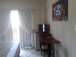 a bedroom with a desk with a television and a window at Fragata Hotel in Guarapari