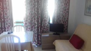 ein Wohnzimmer mit einem TV, einem Tisch und Stühlen in der Unterkunft Apartamentos Mediterraneo in Nerja