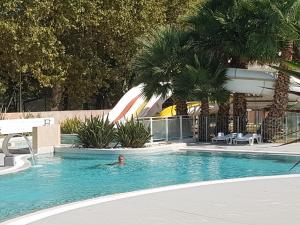 a man swimming in a swimming pool with palm trees at Mobile Home tout confort Séléna in Agde