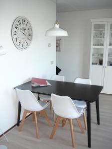 une table à manger noire avec des chaises blanches et une horloge dans l'établissement Strandslag Zanddijk 149 Julianadorp aan Zee, à Julianadorp