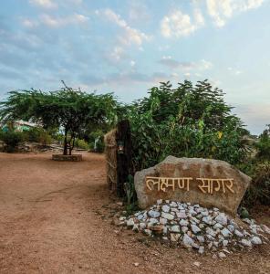 una señal de piedra frente a un arbusto con un árbol en Brij Lakshman Sagar, Pali, en Raipur