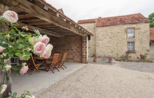 een patio met een tafel en stoelen en roze rozen bij L'Hirondelle in Lantilly
