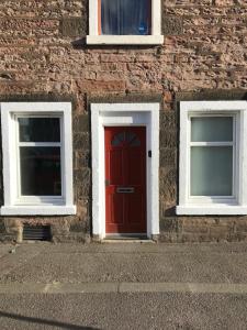 a red door on a brick building with two windows at 2 Lower Kessock Street in Inverness