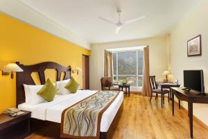 a bedroom with a bed and a desk and a television at Aloha On The Ganges by Leisure Hotels in Rishīkesh
