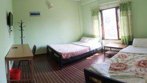 a room with two beds and a table and a desk at Harry Guest House & Restaurant in Pokhara