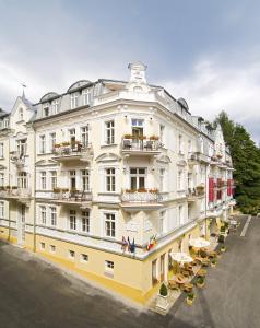 een groot wit gebouw met tafels en stoelen ervoor bij Residence Romanza in Mariánské Lázně