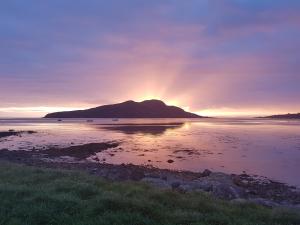 um pôr-do-sol sobre um corpo de água com uma montanha em Bayview Cottage em Lamlash