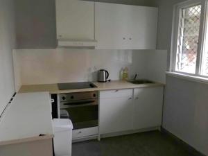 cocina con armarios blancos, fogones y fregadero en Maddington House Unit C en Perth