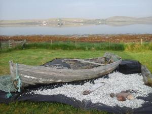 un viejo barco sentado en el césped junto a un lago en The Boat House BED ONLY NO BREAKFAST, en Aultbea