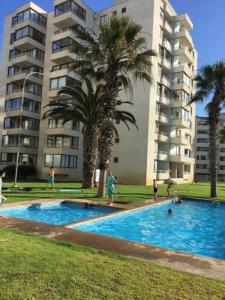 una piscina frente a un edificio con palmeras en DEPTO 1RA LINEA FRENTE AL MAR Condominio Palmar 4P, en La Serena