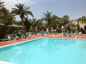 a swimming pool with chairs and palm trees at Baia Delle Palme Beach in Santa Margherita di Pula