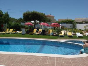 a woman sitting next to a swimming pool with chairs and umbrellas at Sunshine in Albufeira