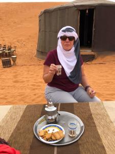 une femme assise à côté d'une table avec une assiette de nourriture dans l'établissement Sahara camel tours camp, à Merzouga